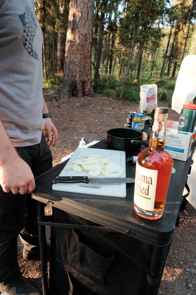 Camp cooking setup with cutting board and gear at a forest campsite in Montana