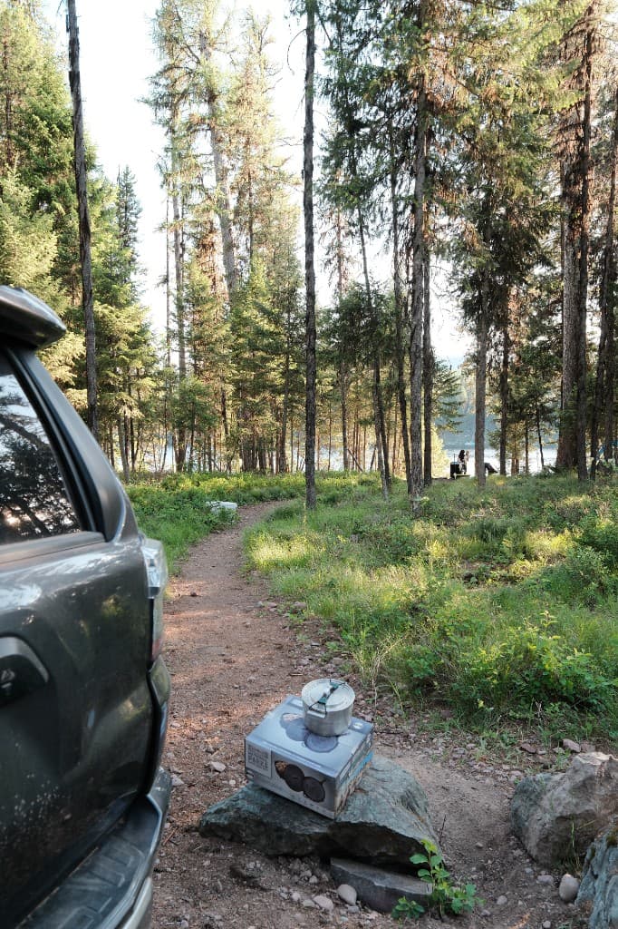 Camping gear and cast iron cookware beside an SUV at a wooded lakeside campsite